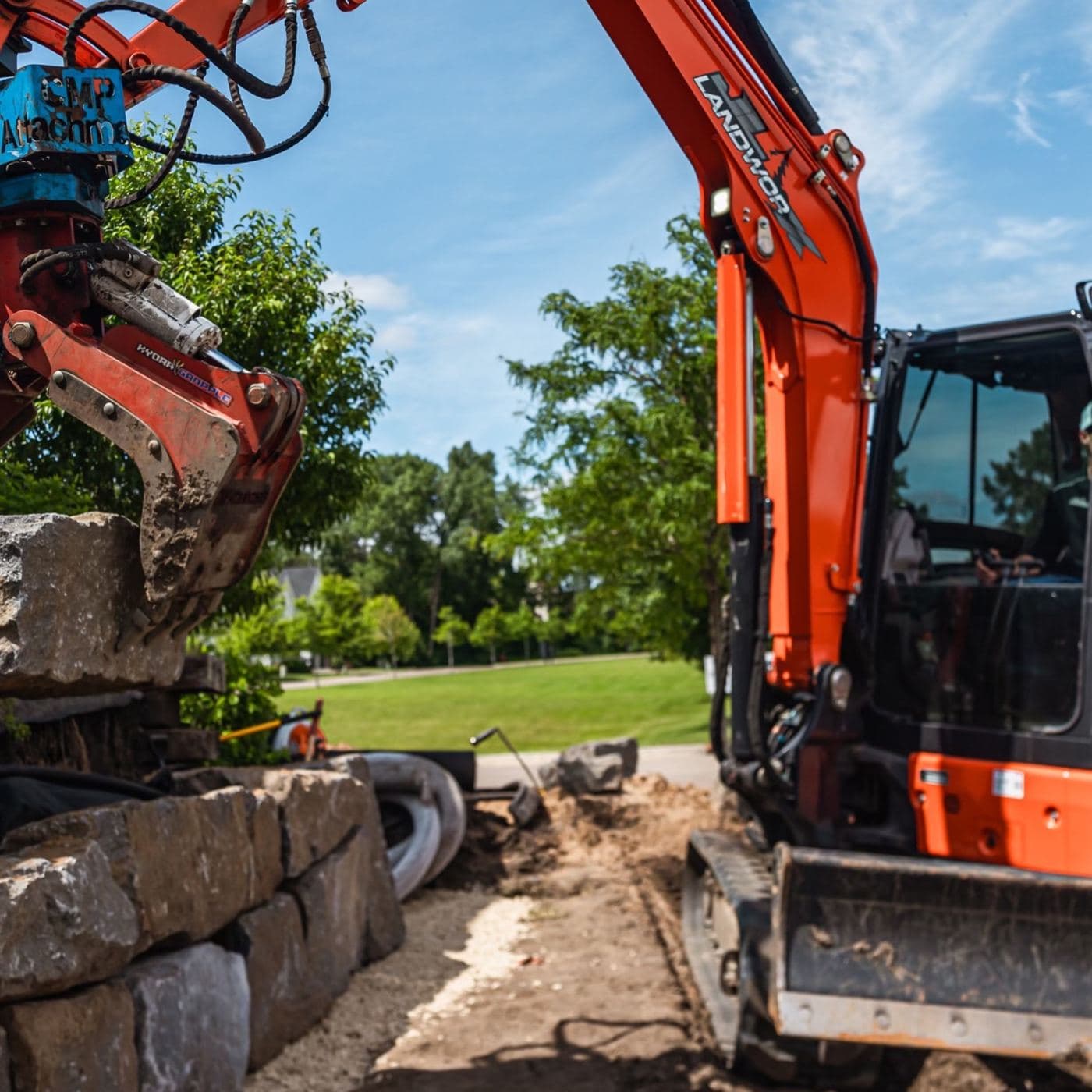 JL Landworx excavator with hydraulic grapple setting limestone blocks on a boulder retaining wall