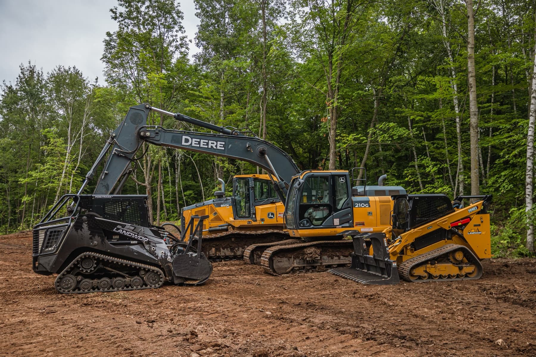 JL Landworx fleet on a cleared homesite: mulcher-equipped track loaders, dozer, and excavator