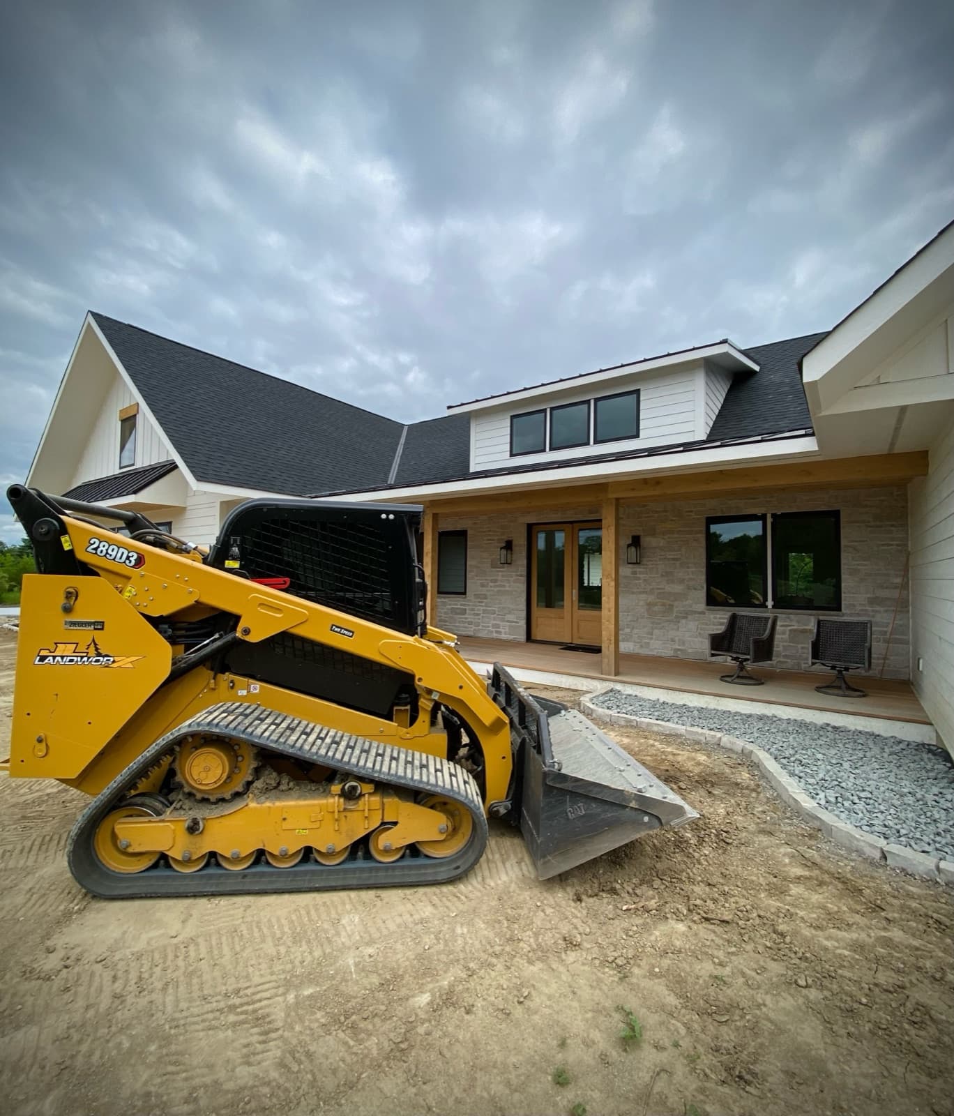 Compact track loader staged for final grading at a newly built farmhouse