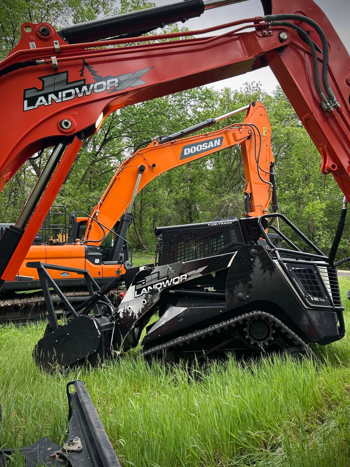 JL Landworx excavators and mulcher-equipped Posi-Track staged in tall grass before clearing