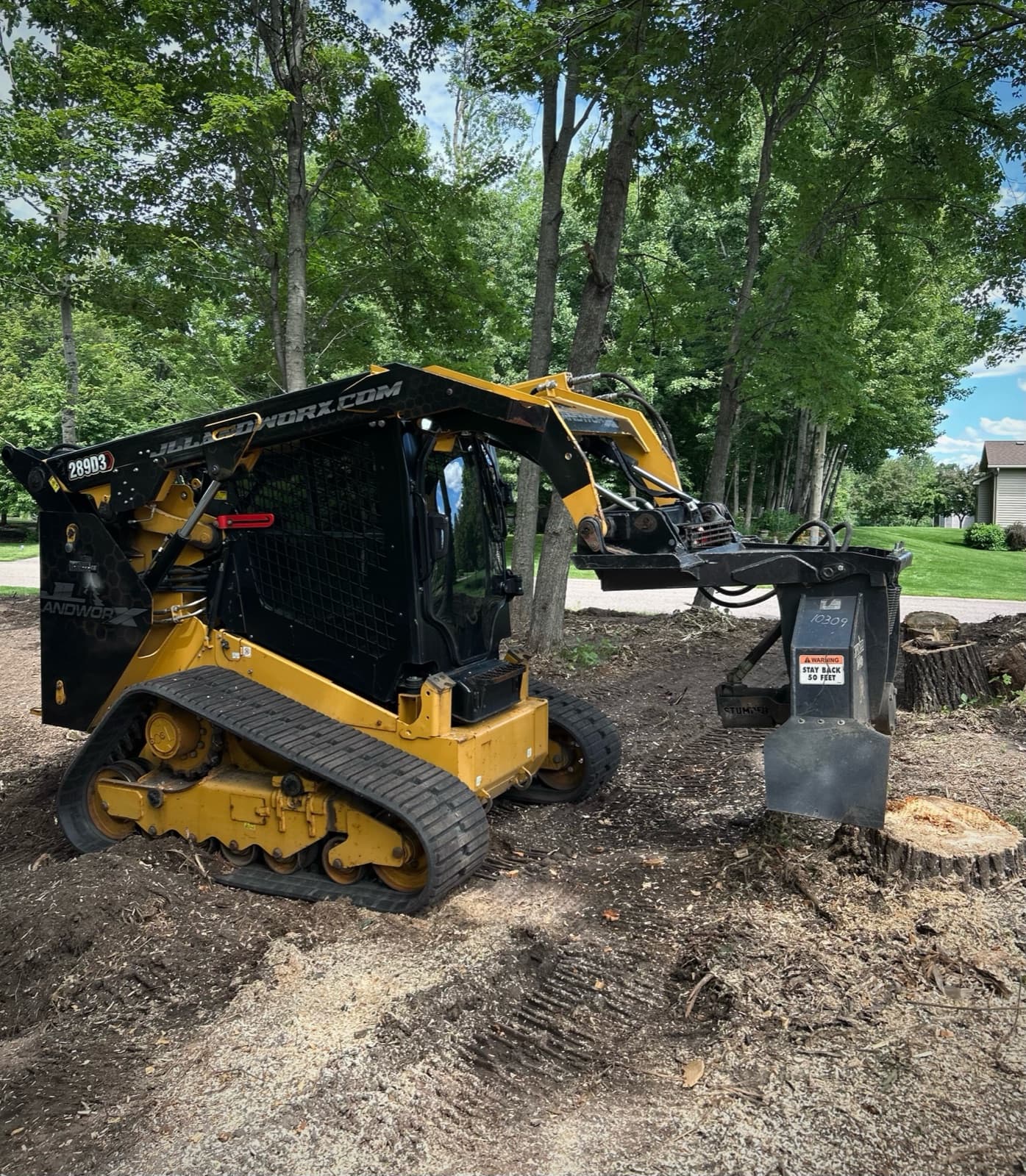 Compact track loader with stump grinder attachment grinding stumps on a residential lot
