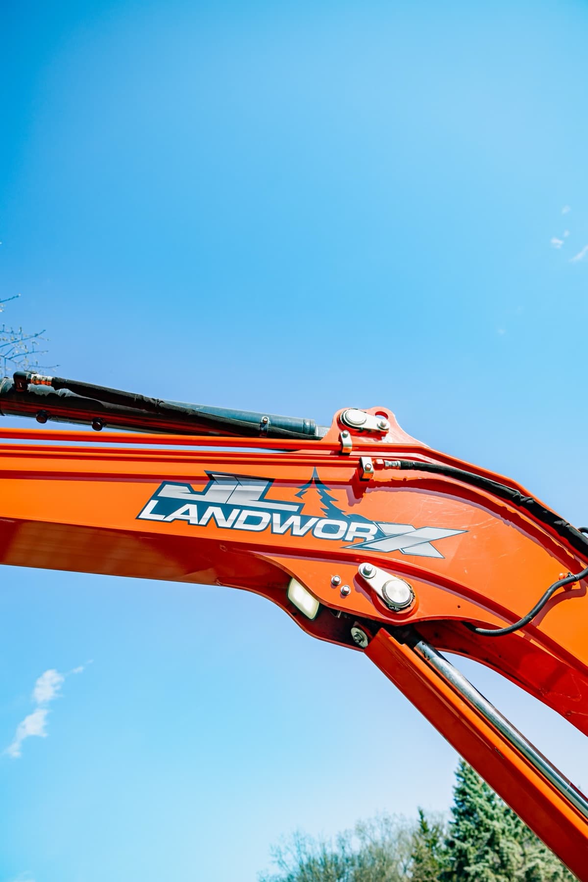 JL Landworx logo on the boom of an excavator against a clear sky