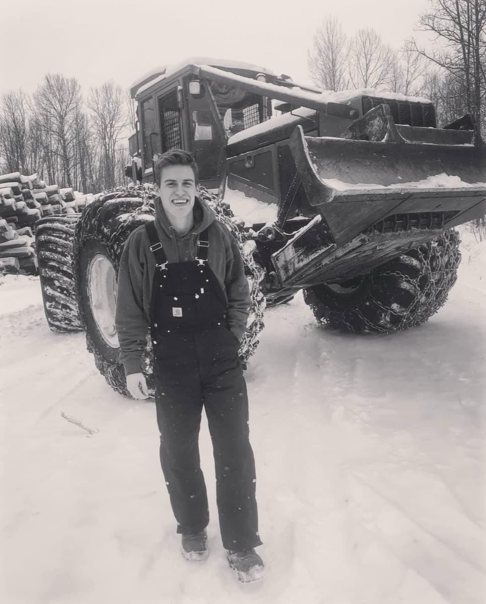 Jordan LaVine on a winter logging job in 2018, in front of a chained-up log skidder