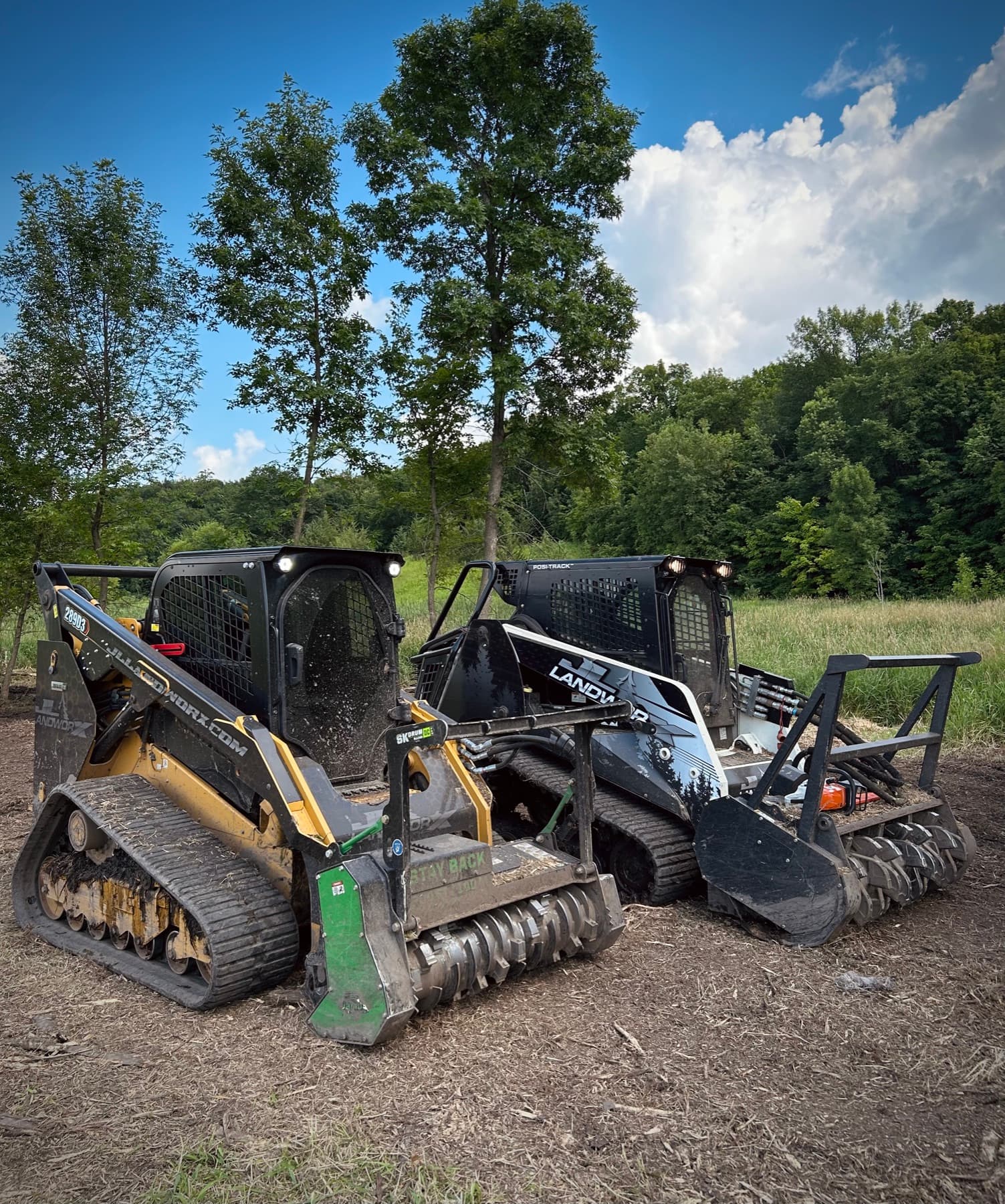 Two JL Landworx compact track loaders with forestry mulcher heads parked on a freshly mulched clearing